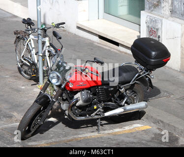 Eine rote Moto Guzzi V7 parkte neben einem Fahrrad gegen ein Schild, Rom, Italien gesichert. Stockfoto