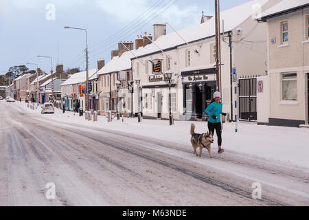 Celbridge, Kildare, Irland. 28 Feb 2018: Irland Wetter. Tier aus dem Osten hits irische Städte. Starker Schneefall in Celbridge. Schnee und Eis sind die Fahrbedingungen erschwert. Frau Joggen mit ihrem Hund auf der Main Street in celbridge. Stockfoto