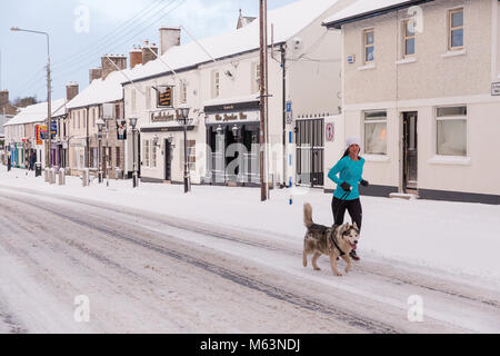 Celbridge, Kildare, Irland. 28 Feb 2018: Irland Wetter. Tier aus dem Osten hits irische Städte. Starker Schneefall in Celbridge. Schnee und Eis sind die Fahrbedingungen erschwert. Frau Joggen mit ihrem Hund auf der Main Street in celbridge. Stockfoto