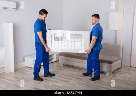 Zwei lächelnde Junge männliche Movers Holding Möbel im Wohnzimmer Stockfoto