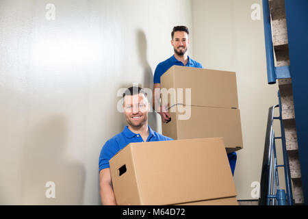 Zwei junge männliche Movers In der blauen Uniform, die Kartons auf Treppe Stockfoto
