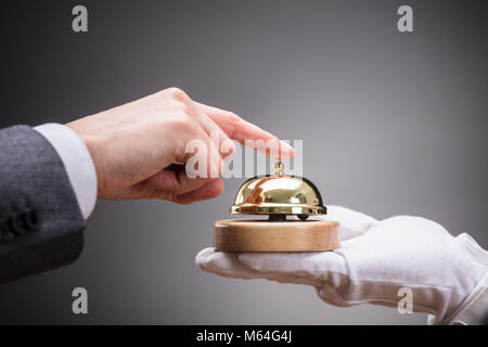 In der Nähe der Person Hand Ringing Service Bell, die Kellner auf grauem Hintergrund Stockfoto