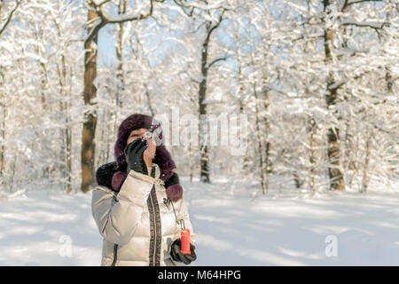 Hält eine Frau eine Handvoll Schnee in den Händen und bläst. Winter im Wald. Die sonne funkelt. Tag, Russland. Stockfoto