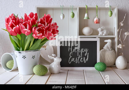 Frühling Hintergrund mit Ostern Dekorationen und eine Kreidetafel. Vitrine mit verschiedenen Objekten und rosa Tulpen. Text "Frohe Ostern" auf der bl Stockfoto