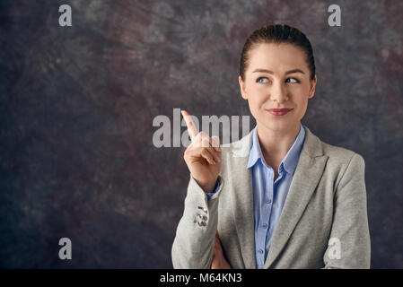 Smart Smiling Young Professional oder Business Frau zeigt mit dem Finger in der Luft mit ein erfreutes Lächeln, als sie eine Lösung für ein Problem findet, oder denkt Stockfoto