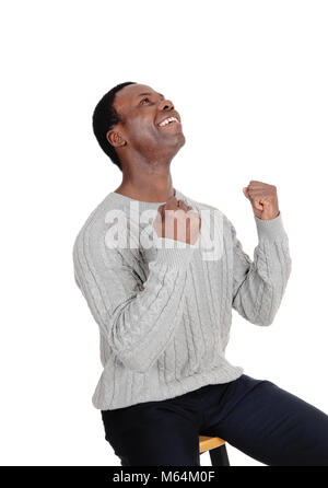 Eine junge schöne afrikanische amerikanische Mann in einem Pullover mit seinen Fäusten sitzen und Lächeln von Sieg und Erfolg, über Weiß isoliert Stockfoto