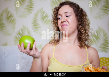 Curly Frau mit einem Apfel und grimasse auf dem Gesicht Stockfoto