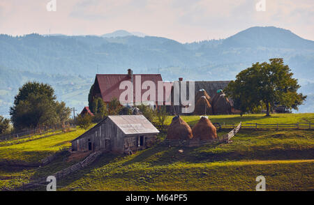 Frühling Landschaft. Traditionelle Siebenbürger Haus mit rustikalen Holzmöbeln Scheune, Stall, hayricks und grünen Weide in Brasov, Rumänien. Stockfoto