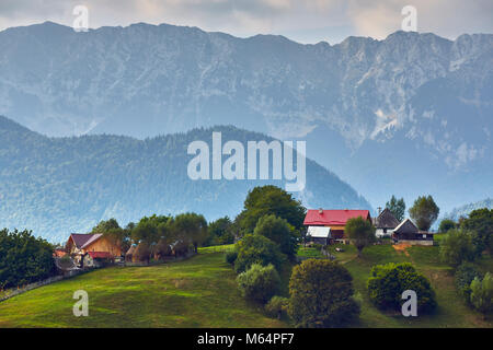 Frühling ländliche Landschaft mit rumänischen Dorf auf einem grünen Hügel in der Nähe von Piatra Craiului Mountain Range, Magura, Brasov County, Siebenbürgen, Rumänien. Stockfoto