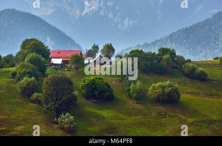 Frühling ländliche Landschaft mit rumänischen Dorf auf einem grünen Hügel in der Nähe von Piatra Craiului Mountain Range, Magura, Brasov County, Siebenbürgen, Rumänien. Stockfoto