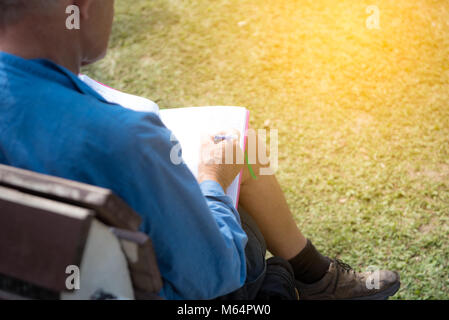 Ein Mann, der allein im Gras Garten sitzen und schreiben Hinweis auf Papier Stockfoto