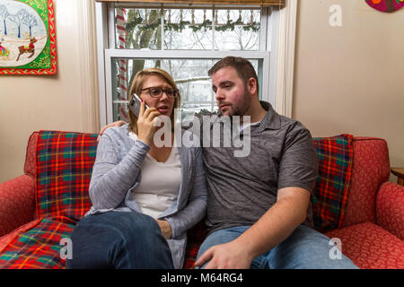 Eine Junge kaukasier Paar wartet aufgeregt und betet für eine gute Nachricht, da Sie sitzen auf Ihren Wohnzimmer Couch. Stockfoto