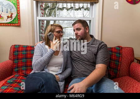 Eine Junge kaukasier Paar wartet aufgeregt und betet für eine gute Nachricht, da Sie sitzen auf Ihren Wohnzimmer Couch. Stockfoto