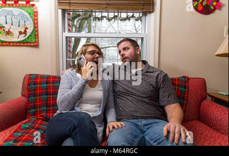 Eine Junge kaukasier Paar wartet aufgeregt und betet für eine gute Nachricht, da Sie sitzen auf Ihren Wohnzimmer Couch. Stockfoto