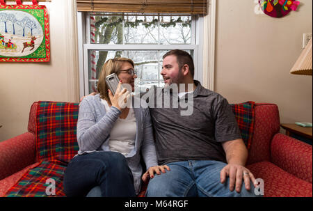 Eine Junge kaukasier Paar wartet aufgeregt und betet für eine gute Nachricht, da Sie sitzen auf Ihren Wohnzimmer Couch. Stockfoto