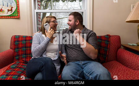 Eine Junge kaukasier Paar wartet aufgeregt und betet für eine gute Nachricht, da Sie sitzen auf Ihren Wohnzimmer Couch. Stockfoto