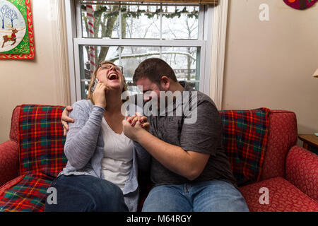 Eine Junge kaukasier Paar wartet aufgeregt und betet für eine gute Nachricht, da Sie sitzen auf Ihren Wohnzimmer Couch. Stockfoto