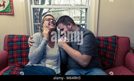 Eine Junge kaukasier Paar wartet aufgeregt und betet für eine gute Nachricht, da Sie sitzen auf Ihren Wohnzimmer Couch. Stockfoto