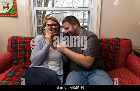 Eine Junge kaukasier Paar wartet aufgeregt und betet für eine gute Nachricht, da Sie sitzen auf Ihren Wohnzimmer Couch. Stockfoto