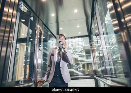 Afroamerican Geschäftsmann in der modernen Aufzug aus Glas am Telefon sprechen Stockfoto