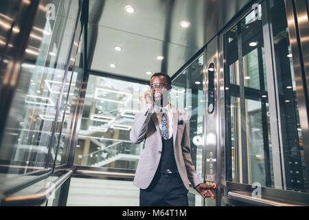 Afroamerican Geschäftsmann in der modernen Aufzug aus Glas am Telefon sprechen Stockfoto