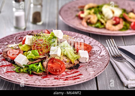 Gesund gemischten Griechischer Salat serviert auf einem rosa Platte mit silbernen Gabel mit gestochen scharfen Blattgemüse, microgreen, Feta, Zwiebeln, Tomaten und Geschnetzeltes Rindfleisch. Sele Stockfoto