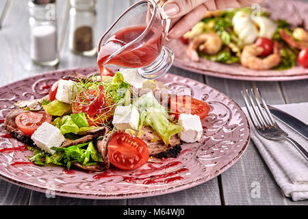 Gesund gemischten Griechischer Salat serviert auf einem rosa Platte mit silbernen Gabel mit gestochen scharfen Blattgemüse, microgreen, Feta, Zwiebeln, Tomaten und Geschnetzeltes Rindfleisch. Sele Stockfoto