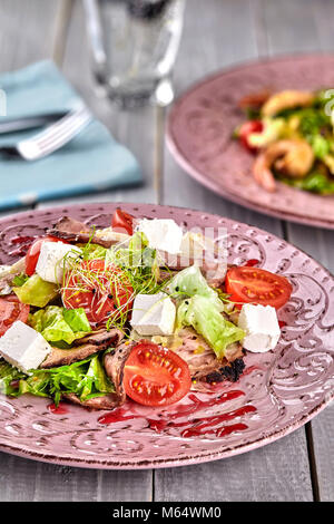 Gesund gemischten Griechischer Salat serviert auf einem rosa Platte mit silbernen Gabel mit gestochen scharfen Blattgemüse, microgreen, Feta, Zwiebeln, Tomaten und Geschnetzeltes Rindfleisch. Sele Stockfoto