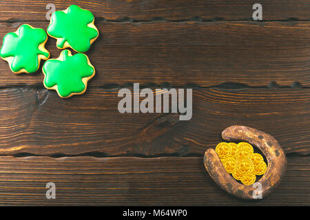Patrick's Day Hintergrund mit Lebkuchen Klee und Hufeisen mit Goldmünzen auf hölzernen Hintergrund Stockfoto