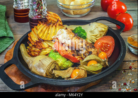 Huhn Kebabs auf Holzspieße mit Brokkoli, Artischocke und Kartoffelchips mit Kräutern in einer Pfanne und ein Holzbrett. Close Up. Stockfoto