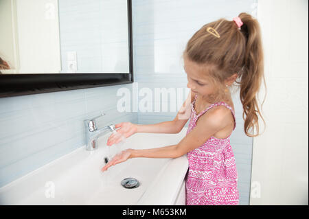 Kleine Mädchen in Kleidung wäscht ihre Hände in das Waschbecken im Badezimmer Stockfoto