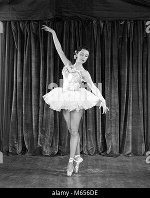 1950 BRUNETTE BALLERINA IN DER KLASSISCHEN POSE AUF POINTE VOR DEM VORHANG AUF DER BÜHNE - d 2459 HAR 001 HARS BRUNETTE PERFORMING ARTS VOR BESETZUNG SCHAUSPIELER KARRIERE TUTU 18-19 JAHRE BALLERINA SLIPPER ENTERTAINER ENTERTAINER SCHAUSPIELER DARSTELLER POSE PRÄZISION JUNGEN ERWACHSENEN FRAU B&W SCHWARZ UND WEISS KAUKASISCHEN ETHNIE ANMUTIGE BERUFE ALTMODISCHE PERSONEN POINTE Stockfoto