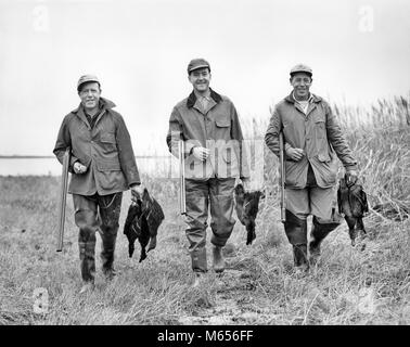 1950 DREI MÄNNER SUCHEN BEI CAMERA HOLDING SCHROTFLINTEN ZU FUSS DURCH GRASARTIGE FEUCHTGEBIETE DIE KLAMMER DER ENTEN-d 3634HAR 001 HARS GLÜCK FRÖHLICHEN ABENTEUER ENTSPANNUNG AUFREGUNG AUSSEN FREIZEIT TRIO STOLZ LÄCHELT FREUDIGE ZUSAMMENARBEIT GRASBEWACHSENEN KLEINEN GRUPPE VON TIEREN, DIE KLEINE GRUPPE VON MENSCHEN FEUERWAFFE FEUERWAFFEN JÄGER MÄNNER Mitte - Mitte - erwachsenen Mann SCHROTFLINTEN FEUCHTGEBIETE B&W SCHWARZ UND WEISS BRACE KAUKASISCHEN ETHNIE DOUBLE BARREL AUF KAMERA ALTMODISCHE PERSONEN Stockfoto