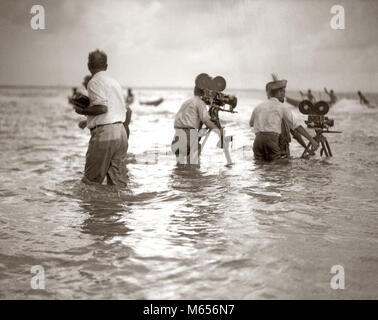 1920 Filmemacher in knietiefem Wasser Meer Dreharbeiten Dreharbeiten Kameras - f 1095 HAR 001 HARS FELSIGE ABENTEUER KARRIERE AUFREGUNG NIEDRIGEN WINKEL KOOPERATION KREATIVITÄT SCHAUSPIELER KAMERALEUTE GRUPPE VON MENSCHEN STUMMFILM MOTION PICTURE WERBUNG NOCH MÄNNER FILM NOCH IMMER SEASCAPE B&W SCHWARZ UND WEISS KAUKASISCHEN ETHNIE KAMERAMANN KAMERALEUTE filmschaffende Berufe ALTMODISCHE OUTRIGGER KANU PERSONEN Stockfoto