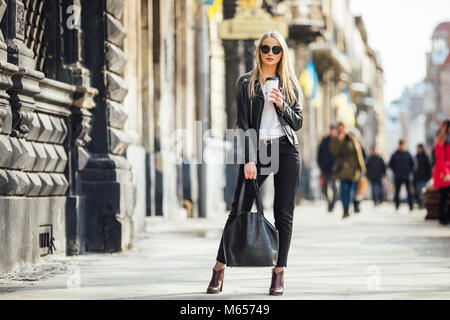 Junge hübsche Mädchen zu Fuß auf der Straße bei einer Tasse Kaffee auf ihre Hand und tragen Sie eine Sonnenbrille, sonnigen Tag Wetter Stockfoto