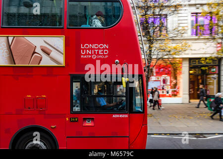 London Bus Fahrer in seiner Kabine fahren Sie auf der Oxford Street, während ein Mann sitzt auf dem obersten Deck auf der Vorderseite für Kopfhörer hört, Oxford Street, London, UK Stockfoto