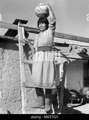 1930er Jahre native american Indian FRAU AUF LEITER HOLDING OLLA KERAMIK KRUG AUF DEM KOPF COCHITI PUEBLOS NEW MEXICO USA-i 1483 HAR 001 HARS NORDAMERIKA JAR 25-30 Jahre 30-35 JAHRE NORDAMERIKANISCHEN STÄRKE LOW ANGLE STOLZ NATIVE AMERICAN PUEBLO COCHITI MITTE NACH MITTE DER ERWACHSENEN FRAU NEW YORK B&W SCHWARZ UND WEISS EINHEIMISCHE BERUFE ALTMODISCHE OLLA PERSONEN POTTER Stockfoto