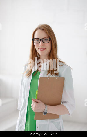 Porträt eines lächelnden jungen Ärztin mit medizinischen Kleid und Zwischenablage. Gute Gesundheitsversorgung Konzept Stockfoto