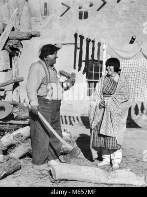 1930er Jahre NATIVE AMERICAN PAAR FRAU IN TYPISCHEN KOSTÜM MANN IN JEANS ZERKLEINERN VON BRENNHOLZ MIT AX SAN ILDEFONSO PUEBLO COLORADO USA-i 1648 HAR 001 HARS KOPIE RAUM FREUNDSCHAFT IN VOLLER LÄNGE DAMEN INDER PAARE AMERICANA Nostalgie im mittleren Alter Mann im mittleren Alter AX UFER FRAUEN GLÜCK Frau mittleren Alters heiter LÄCHELT FRÖHLICH KULTUR INDIANISCHE PUEBLO SAN ILDEFONSO ADOBE HACKEN ERBE MÄNNER NEUE MEXIKO TYPISCHE B&W SCHWARZ UND WEISS BRENNHOLZ ILDEFONSO NM ALTMODISCHE PERSONEN Stockfoto