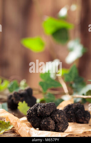 Schwarze Trüffeln und Blätter auf alten Holztisch. Stockfoto