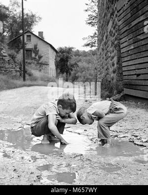 1950er Jahre 1960er Jahre zwei jungen BIEGEN SIE AM spielen in der SCHLAMMPFÜTZE-j 11747 HAR 001 HARS INSPIRATION VEREINIGTE STAATEN VON AMERIKA GESCHWISTER NOSTALGIE 3-4 JAHRE BIEGEN TRÄUME GLÜCK ABENTEUER DISCOVERY AUFREGUNG WISSEN WACHSTUM GESCHWISTER ZUSAMMENARBEIT SCHLAMM IDEEN JUGENDLICHE MÄNNER FRAGEN B&W SCHWARZ UND WEISS KAUKASISCHEN ETHNIE erkunden neugierig UNTERSUCHT ALTMODISCHE PFÜTZE REGENWASSERS Stockfoto