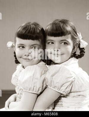 1940s 1950s TWIN Mädchen lächelnd umarmen - j 1832 HAR 001 HARS GESCHWISTER SCHWESTERN NOSTALGIE ZWEISAMKEIT 3-4 JAHRE BRUNETTE PASSENDE GLEICHEN 5-6 JAHRE GLÜCK UNTERSTÜTZUNG UNTERSCHIED WACHSTUM GESCHWISTER LÄCHELT VERBINDUNG FREUDIGE ZUSAMMENARBEIT - GEFLECHTE DOPPELTE GRINSEN JUGENDLICHE SEHEN GLEICH ZOPF ZÖPFE GLEICHERMASSEN B&W BANGS größere schwarze und weiße KAUKASISCHEN ETHNIE CLONE AUF SEITE ALTMODISCHE GLEICHHEIT KLEINER ZWEI PERSONEN MIT ANDEREN Stockfoto