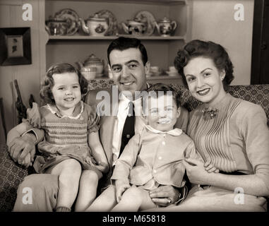 1950 s Familie sitzt auf der WOHNZIMMER COUCH zusammen lächeln in die Kamera-j 3908 HAR 001 HARS ZUKUNFT BRUDER OLD FASHION SCHWESTER KINDER COUCH STIL KAUKASISCHEN SÖHNE FREUEN FREUDE LIFESTYLE FRAUEN BRÜDER GROWNUP HOME LIFE COPY SPACE MENSCHEN KINDER HALBE LÄNGE DAMEN TÖCHTER GROWN-UP PFLEGE ZUHAUSE GESCHWISTER VERTRAUEN SCHWESTERN FAMILIEN NOSTALGIE VÄTER MITEINANDER 1-2 Jahre 25-30 JAHRE 3-4 JAHRE 30-35 JAHRE GLÜCK WOHNZIMMER MAMMEN VATIS STOLZ GESCHWISTER LÄCHELT FRÖHLICH KLEINE GRUPPE VON MENSCHEN jugendliche Männer Mitte - Mitte - erwachsenen Mann Mitte der erwachsenen Frau B&W SCHWARZ UND WEISS KAUKASISCHEN ETHNIE Stockfoto