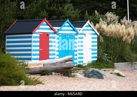 Drei Strandhütten mit blauen Streifen am Rand von einem Strand in Großbritannien. Stockfoto