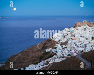 Einer geschmeidigen Straße nach Chora von Astypalea in der blauen Stunde und der Vollmond vom Horizont Stockfoto