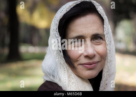 Porträt der reifen Frau, die ihren Kopf mit Hijab Stil weißen Schal im Park. Junge Frau mit weißem Schleier über Kopf, muslimischen suchen Stockfoto