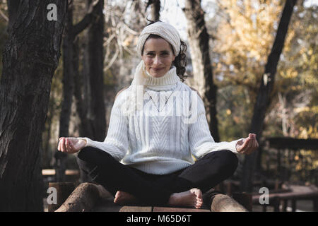 Im mittleren Alter gut aussehende Yogalehrerin in Lotus aufwerfen, wie padmasana bekannt, auf Holz- der Weg in den Park im Herbst Saison. Natur Anschlusskonzept Stockfoto