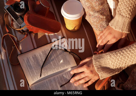 Woman's Hände mit retro Foto Kamera in Braun Leder und ein Buch und Kaffee im Herbst Stockfoto