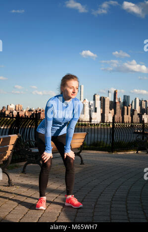 Sport und Fitness. Müde Frau Runner eine Pause nach dem Hart im Park mit Blick auf Downtown Manhattan New York City. Stockfoto