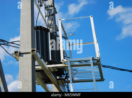 Eine elektrische Verteilung Transformator mit Kühlrippen auf der Pole. Gegen den blauen Himmel. Seitenansicht Stockfoto